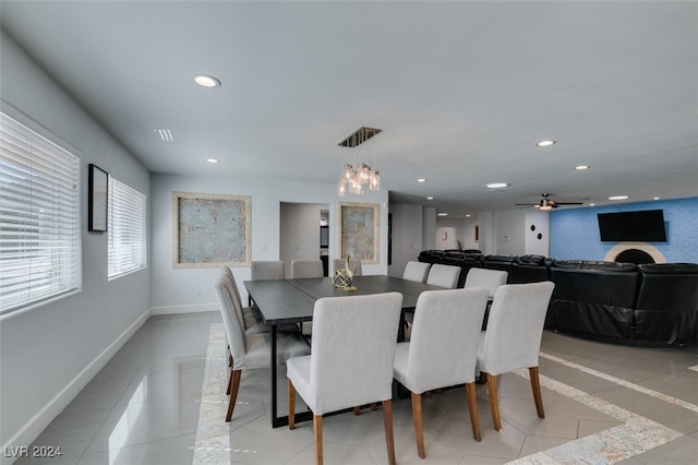 dining room featuring a brick fireplace, ceiling fan with notable chandelier, and light tile patterned floors