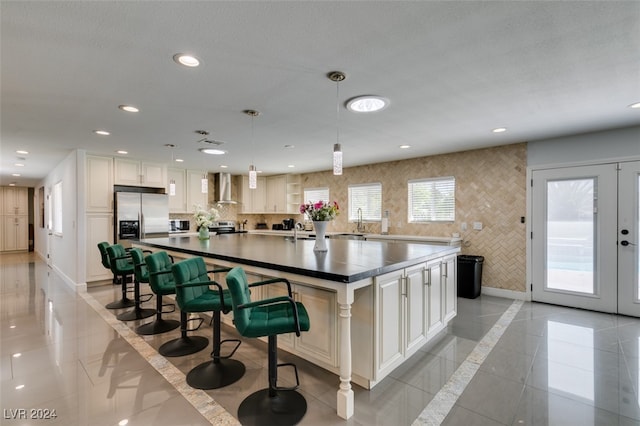 kitchen featuring a center island, wall chimney exhaust hood, hanging light fixtures, light tile patterned flooring, and appliances with stainless steel finishes