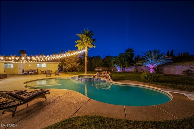 pool at night with a patio and an in ground hot tub