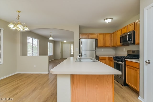 kitchen with light wood-type flooring, appliances with stainless steel finishes, sink, and an island with sink