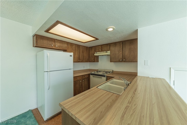 kitchen featuring sink, kitchen peninsula, a textured ceiling, white appliances, and light wood-type flooring