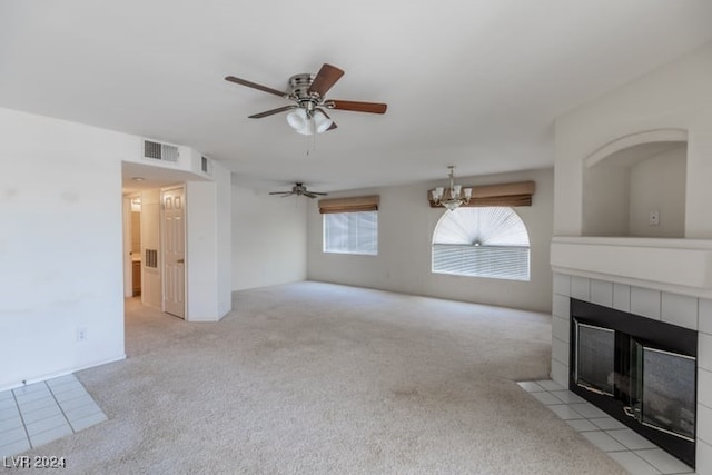 unfurnished living room featuring light colored carpet, a tiled fireplace, and ceiling fan with notable chandelier