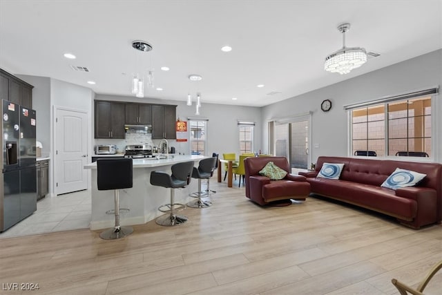 kitchen featuring hanging light fixtures, light wood-type flooring, black fridge, and a kitchen island with sink