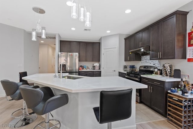 kitchen featuring a kitchen island with sink, sink, light wood-type flooring, decorative light fixtures, and stainless steel appliances