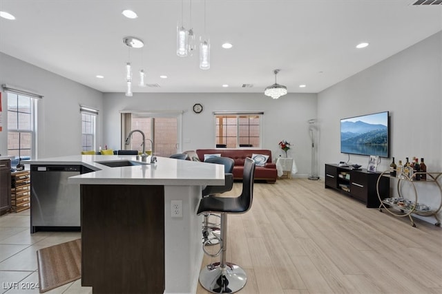 kitchen with pendant lighting, dishwasher, a center island with sink, sink, and light hardwood / wood-style flooring