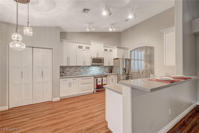 kitchen with kitchen peninsula, appliances with stainless steel finishes, backsplash, white cabinets, and lofted ceiling