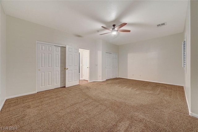 unfurnished bedroom featuring ceiling fan, carpet floors, and two closets