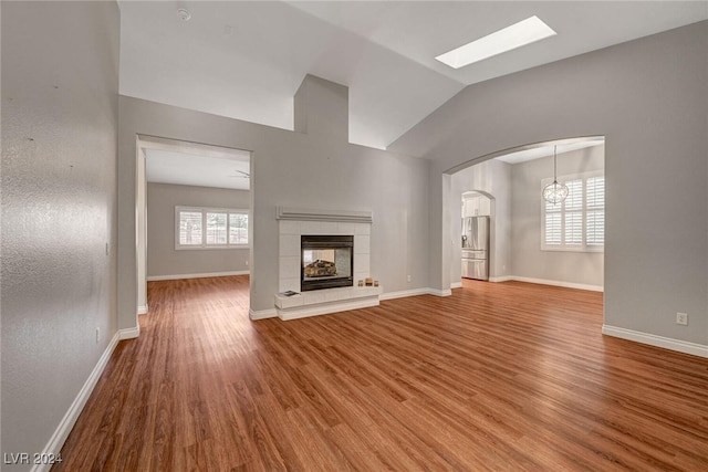 unfurnished living room featuring hardwood / wood-style floors, a healthy amount of sunlight, lofted ceiling, and a tile fireplace