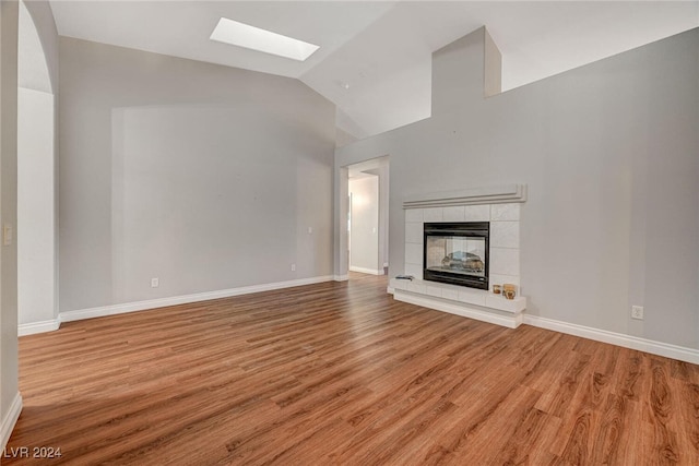 unfurnished living room featuring a tile fireplace, lofted ceiling with skylight, and light hardwood / wood-style flooring