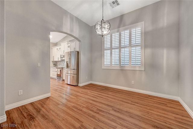 spare room with a chandelier, lofted ceiling, and light wood-type flooring