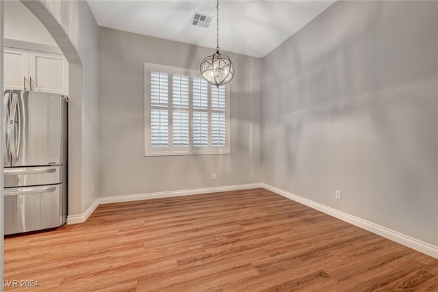 unfurnished dining area featuring light wood-type flooring and a notable chandelier