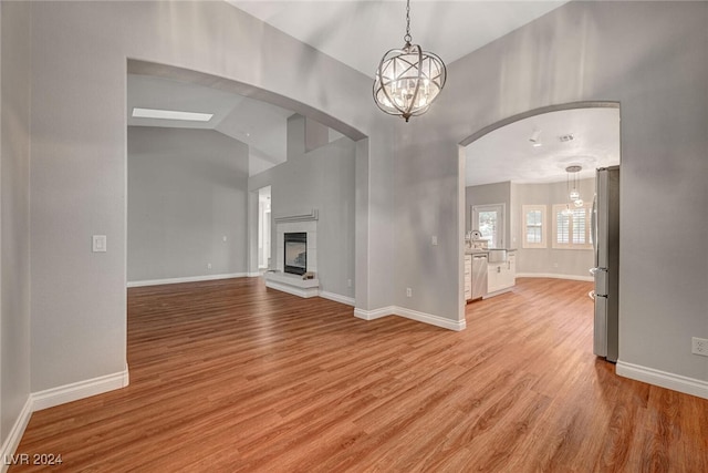 unfurnished living room with sink, light hardwood / wood-style floors, vaulted ceiling, and a notable chandelier