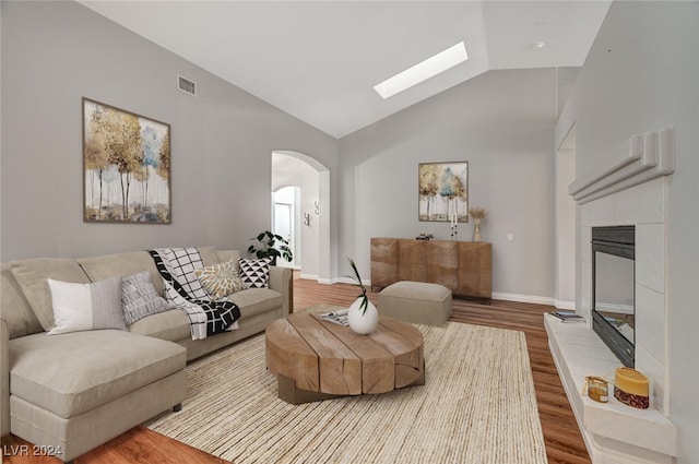 living room with a tiled fireplace, vaulted ceiling, and hardwood / wood-style flooring