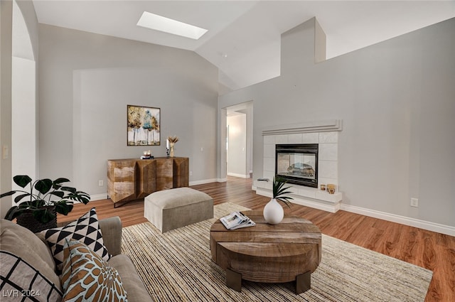 living room featuring a tiled fireplace, vaulted ceiling with skylight, and wood-type flooring