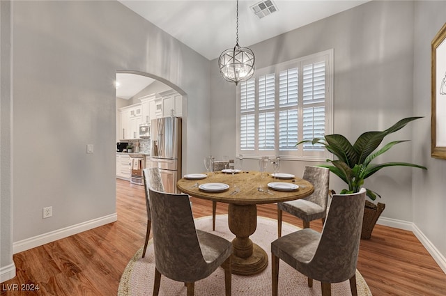 dining space featuring light wood-type flooring, an inviting chandelier, and lofted ceiling