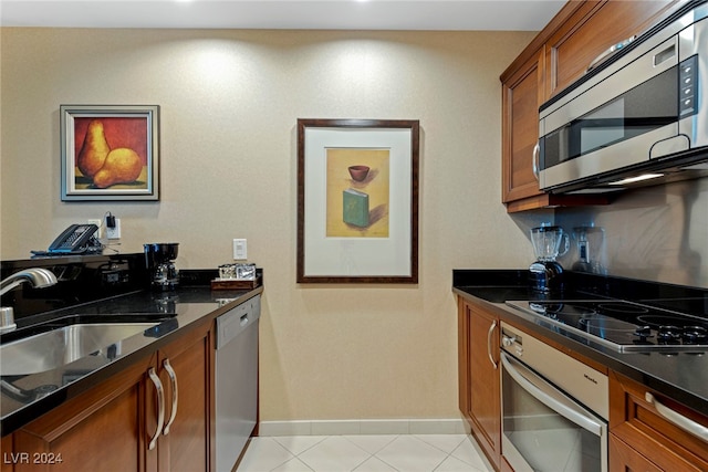 kitchen with stainless steel appliances, light tile patterned flooring, dark stone countertops, and sink