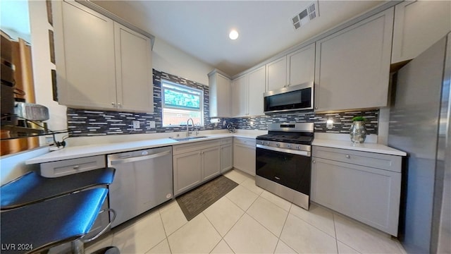 kitchen featuring stainless steel appliances, decorative backsplash, sink, light tile patterned floors, and gray cabinets