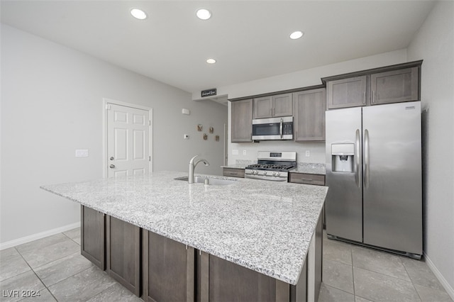 kitchen featuring sink, an island with sink, dark brown cabinets, light stone counters, and stainless steel appliances