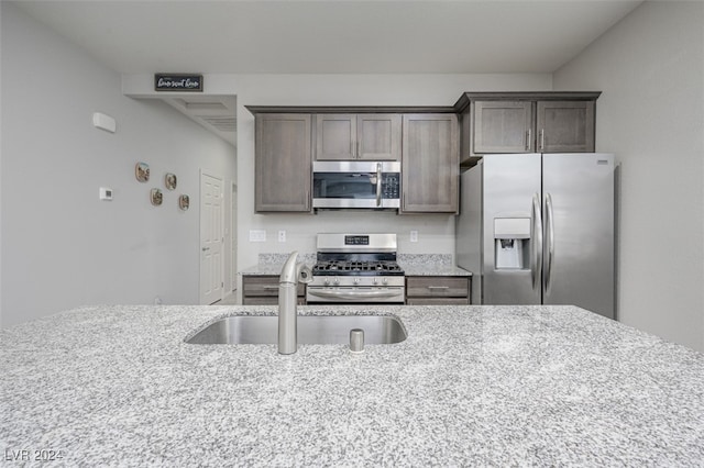 kitchen with light stone countertops, appliances with stainless steel finishes, dark brown cabinetry, and sink