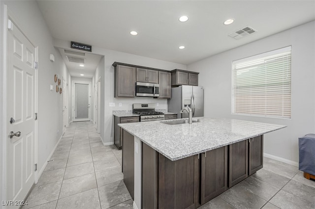 kitchen with light stone countertops, dark brown cabinets, stainless steel appliances, sink, and an island with sink