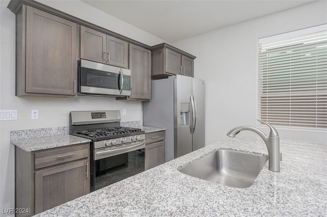 kitchen with light stone countertops, appliances with stainless steel finishes, dark brown cabinetry, and sink