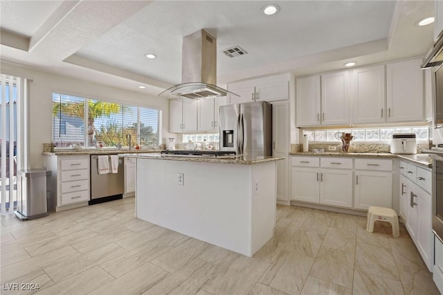 kitchen with island exhaust hood, stainless steel appliances, a raised ceiling, a kitchen island, and white cabinetry