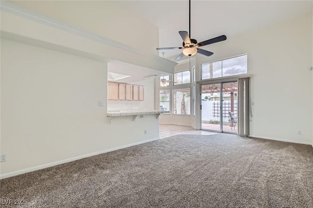 unfurnished living room featuring light colored carpet, baseboards, a high ceiling, and a ceiling fan