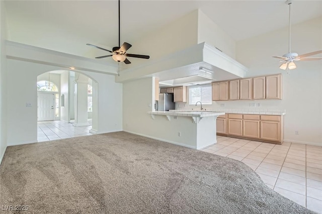 interior space with light carpet, light brown cabinets, a sink, freestanding refrigerator, and a breakfast bar area