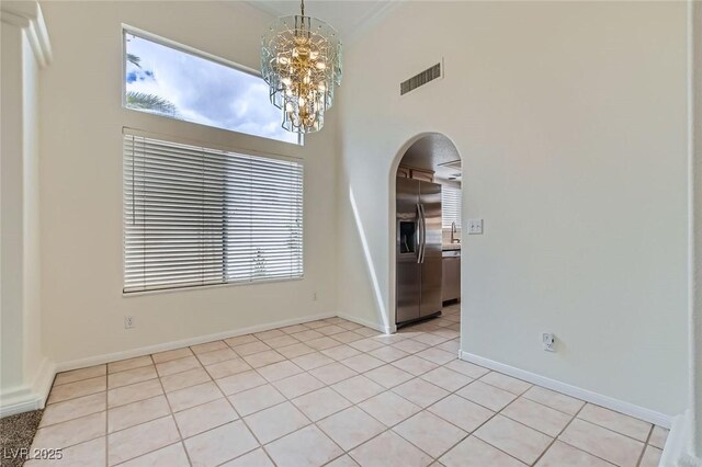 empty room with visible vents, arched walkways, light tile patterned floors, baseboards, and a chandelier