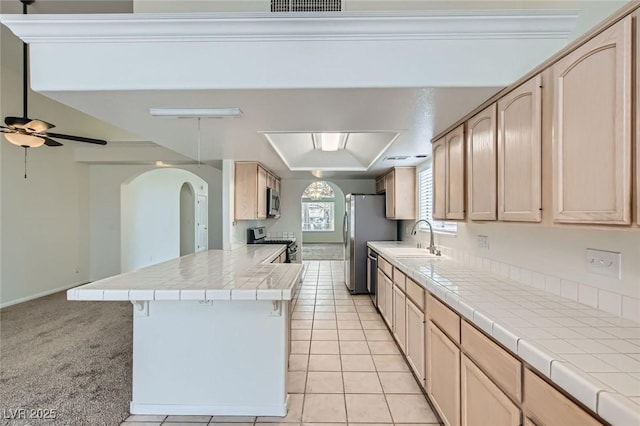 kitchen featuring appliances with stainless steel finishes, a peninsula, arched walkways, a ceiling fan, and a sink