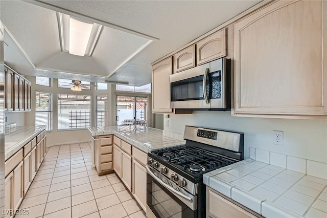 kitchen with stainless steel appliances, a peninsula, tile counters, and light brown cabinets