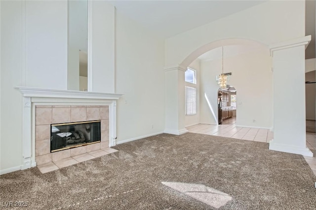 unfurnished living room with carpet flooring, baseboards, arched walkways, and a tile fireplace