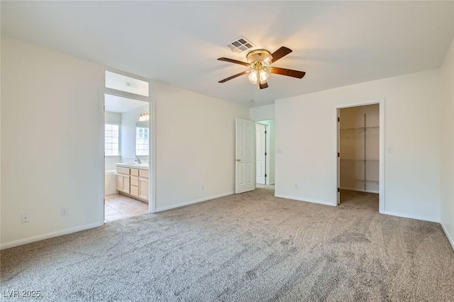 unfurnished bedroom featuring a spacious closet, visible vents, connected bathroom, baseboards, and light colored carpet