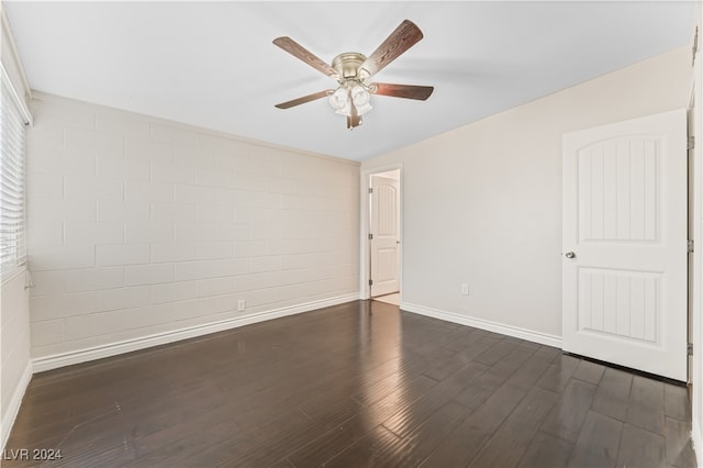 spare room featuring ceiling fan, dark hardwood / wood-style flooring, and brick wall