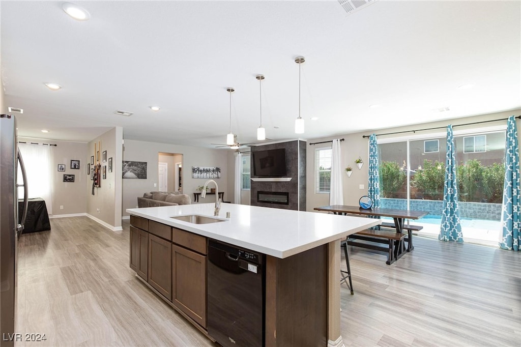 kitchen with sink, hanging light fixtures, light hardwood / wood-style flooring, black dishwasher, and an island with sink