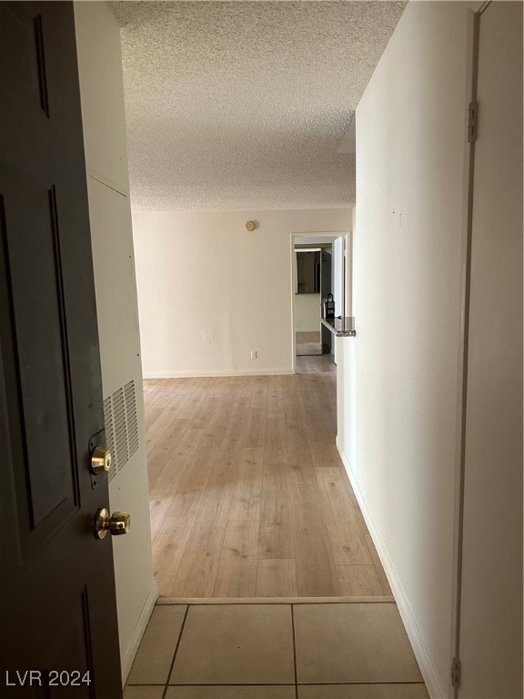 corridor with light wood-type flooring and a textured ceiling