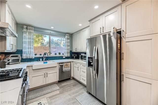 kitchen featuring stainless steel appliances, sink, light stone countertops, backsplash, and light hardwood / wood-style flooring