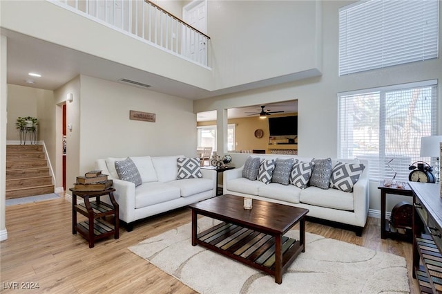 living room featuring light wood-type flooring, a towering ceiling, plenty of natural light, and ceiling fan