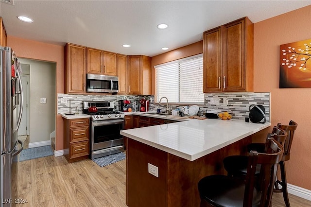 kitchen featuring kitchen peninsula, decorative backsplash, stainless steel appliances, and light hardwood / wood-style flooring