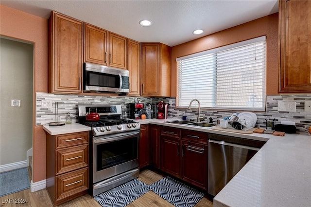 kitchen featuring tasteful backsplash, sink, light hardwood / wood-style flooring, and appliances with stainless steel finishes