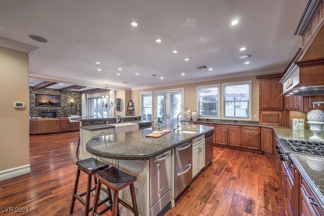 kitchen with dark hardwood / wood-style flooring, a breakfast bar, sink, a large island with sink, and a stone fireplace