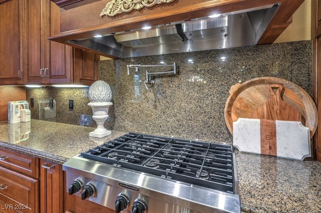 kitchen featuring tasteful backsplash, stainless steel gas cooktop, dark stone countertops, and exhaust hood