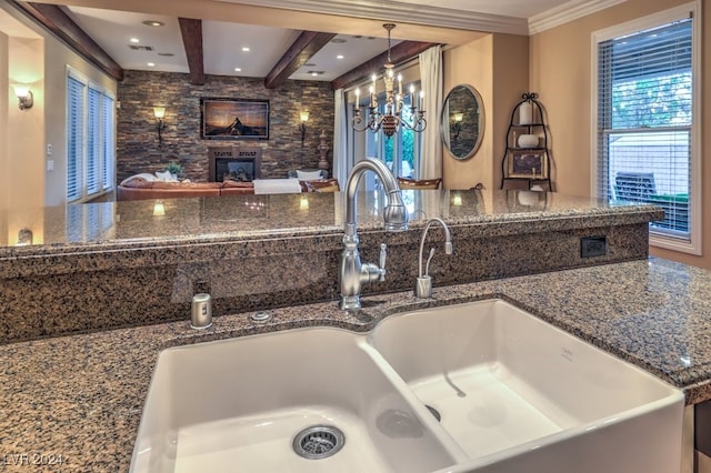 kitchen featuring sink, hanging light fixtures, dark stone countertops, crown molding, and a fireplace