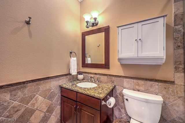 bathroom featuring vanity, toilet, and tile walls