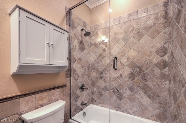 bathroom with toilet, tile walls, and bath / shower combo with glass door