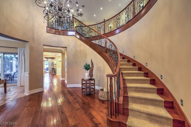 stairs with wood-type flooring, a high ceiling, and a notable chandelier