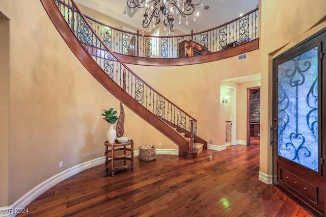 foyer entrance featuring hardwood / wood-style floors, a towering ceiling, crown molding, and a chandelier