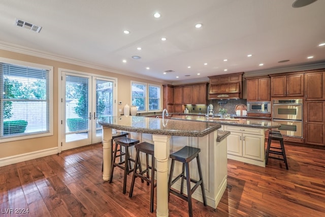 kitchen with appliances with stainless steel finishes, a breakfast bar, dark hardwood / wood-style floors, and a large island with sink