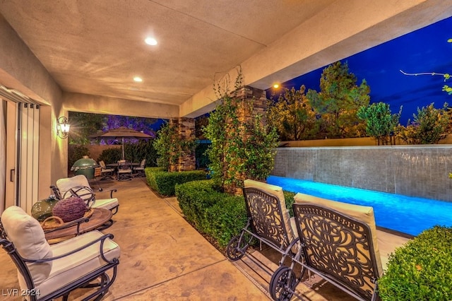 patio at night featuring area for grilling and a pool