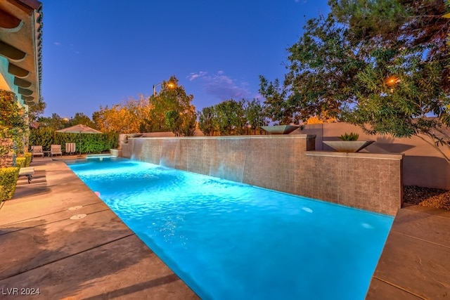 pool at dusk featuring pool water feature and a patio area